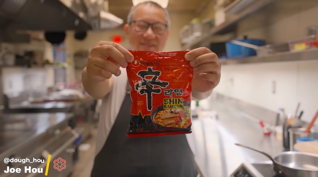 Chef Joe Hou holding up a pack of Shin Ramyun in a restaurant kitchen