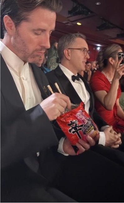 Co-director Chris Appelhans eating Shin Ramyun from the bag in a tuxedo at the Oscars