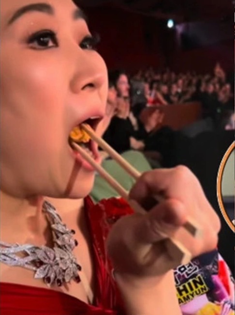 Director Maggie Kang eating dry Shin Ramyun with chopsticks in her seat at the Oscars